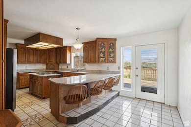 Kitchen featuring light stone countertops, a kitchen breakfast bar, decorative light fixtures, a peninsula, and backsplash