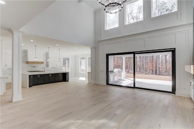 Unfurnished living room with a chandelier, healthy amount of natural light, light wood finished floors, recessed lighting, and ornate columns