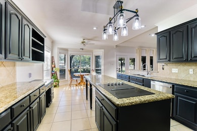 Kitchen featuring decorative backsplash, dark cabinetry, hanging light fixtures, light stone countertops, and light tile patterned floors