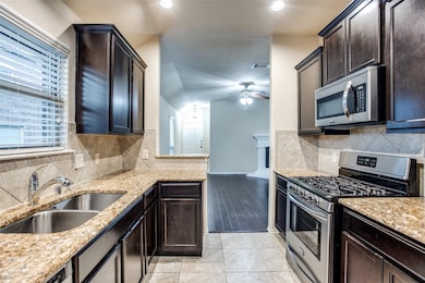 Kitchen with stainless steel appliances, light stone countertops, backsplash, dark brown cabinetry, and ceiling fan
