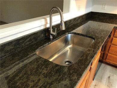Kitchen view of a sink, dark stone countertops, light wood-type flooring, and brown cabinetry