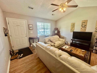 Living area featuring wood finished floors, a ceiling fan, vaulted ceiling, and a textured ceiling