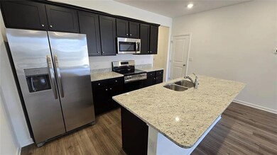 Kitchen featuring stainless steel appliances, dark cabinets, a sink, a center island with sink, and dark wood-style flooring
