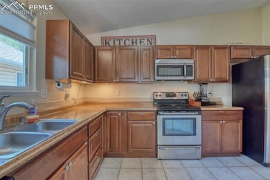 Kitchen featuring stainless steel appliances, lofted ceiling, light tile patterned floors, light countertops, and brown cabinetry