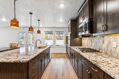 Kitchen with dark brown cabinets, hanging light fixtures, light stone counters, light wood-type flooring, and a textured ceiling
