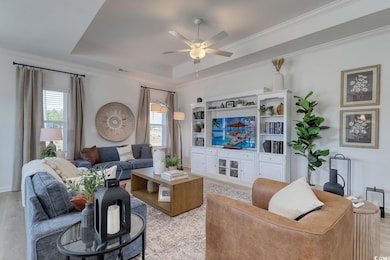 Living area with plenty of natural light, a ceiling fan, crown molding, a raised ceiling, and light wood-type flooring