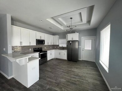 Kitchen with white cabinetry, appliances with stainless steel finishes, decorative light fixtures, dark hardwood / wood-style floors, and kitchen peninsula