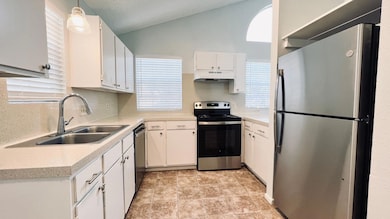 Kitchen featuring appliances with stainless steel finishes, white cabinets, backsplash, under cabinet range hood, and decorative light fixtures