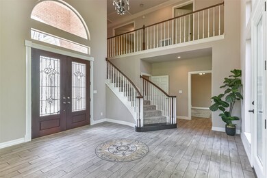Another view of the foyer showcases the beautiful mahogany double doors with leaded glass detailing, topped by a palladium arched window. Also note the sweeping staircase to the second-floor landing and the master suite tucked just behind the staircase.