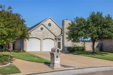 French country home featuring driveway, a garage, brick siding, and a chimney