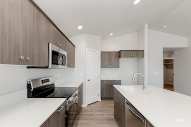 Kitchen with stainless steel appliances, modern cabinets, light wood-style flooring, vaulted ceiling, and light stone countertops