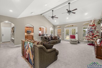 Living room with arched walkways, light colored carpet, ceiling fan, beam ceiling, and high vaulted ceiling