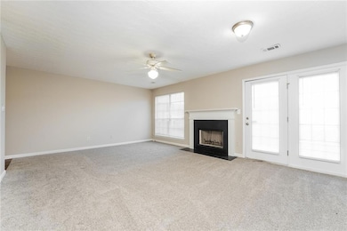 Unfurnished living room featuring light colored carpet, a fireplace with flush hearth, and a ceiling fan