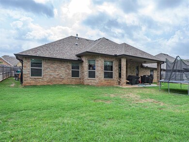 Rear view of house featuring a trampoline, a patio, a shingled roof, and brick siding