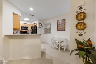 Kitchen featuring light brown cabinets, light tile patterned floors, black appliances, light stone countertops, and a peninsula