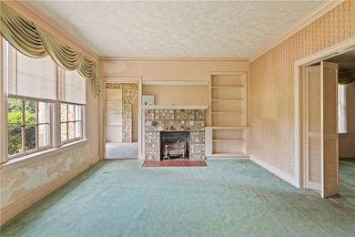 Unfurnished living room featuring wallpapered walls, carpet, a fireplace, baseboards, and crown molding