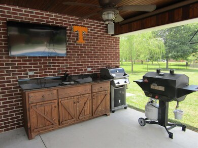 The covered patio of pool house has a ceiling fan & custom built-in cabinets with sink. 
