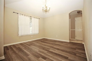 Unfurnished room with a chandelier, dark wood-type flooring, and arched walkways