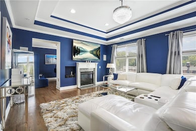 Living area with healthy amount of natural light, wood finished floors, crown molding, a tray ceiling, and a high end fireplace