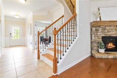 Foyer entrance with crown molding, stairs, a stone fireplace, a wainscoted wall, and a decorative wall