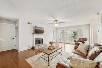 Living room featuring wood finished floors, ceiling fan, a glass covered fireplace, baseboards, and a textured ceiling
