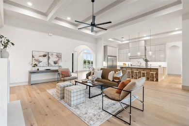 Living room featuring arched walkways, beam ceiling, light wood-style floors, a tray ceiling, and a ceiling fan