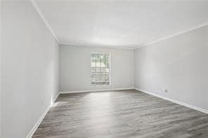 Spare room with wood finished floors, crown molding, and baseboards
