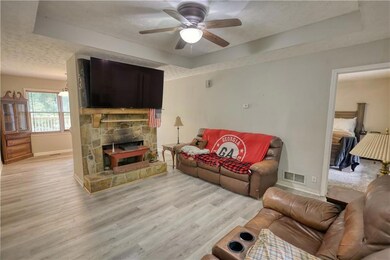 Living room featuring a tray ceiling, baseboards, a textured ceiling, light wood-style flooring, and a ceiling fan