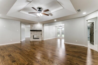 Living Room with a stone  see thru fireplace, ceiling fan with notable chandelier, dark hardwood / wood-style floors, and a raised ceiling