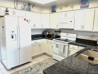 Kitchen with white appliances, light tile patterned flooring, a sink, and white cabinetry
