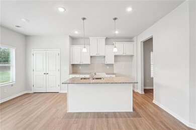 Kitchen with an island with sink, light wood-style floors, tasteful backsplash, white cabinetry, and recessed lighting