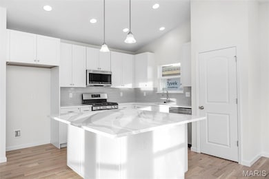 Kitchen featuring a kitchen island, hanging light fixtures, decorative backsplash, white cabinetry, and appliances with stainless steel finishes