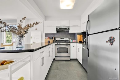 Kitchen featuring appliances with stainless steel finishes, decorative backsplash, white cabinetry, extractor fan, and a peninsula