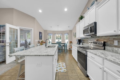 Kitchen featuring a kitchen bar, stainless steel appliances, white cabinetry, backsplash, and a center island with sink
