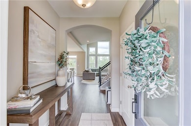 Entryway with arched walkways, dark wood-type flooring, and stairway