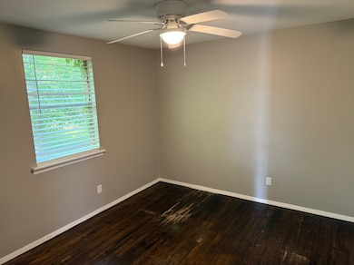 Empty room featuring a ceiling fan, dark wood finished floors, and baseboards