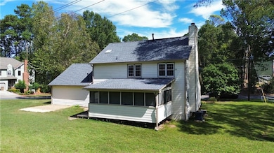 Rear view of property with a sunroom, a chimney, a yard, and roof with shingles