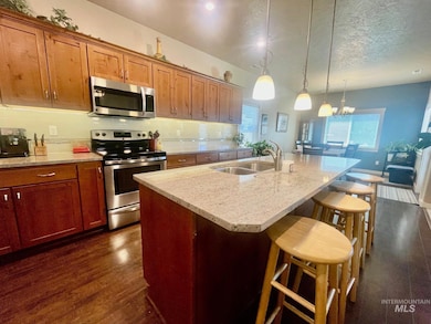 Kitchen featuring appliances with stainless steel finishes, a kitchen bar, a center island with sink, backsplash, and dark wood finished floors