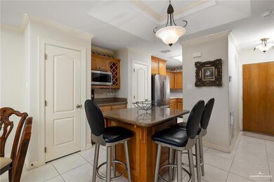 Kitchen with stainless steel appliances, light tile patterned floors, a kitchen island, a kitchen breakfast bar, and brown cabinetry