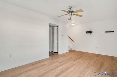 Unfurnished living room featuring light wood finished floors, a ceiling fan, and stairs