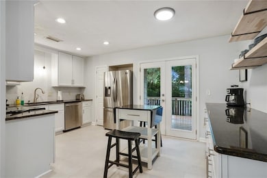 Kitchen with stainless steel appliances, french doors, white cabinets, a sink, and tasteful backsplash