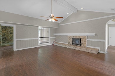 Unfurnished living room with a fireplace, a wainscoted wall, beam ceiling, ceiling fan, and dark wood-type flooring