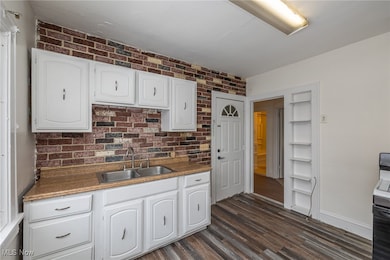 Kitchen with white cabinetry, vinyl plank floors, stove, and brick wall