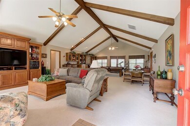 Living room featuring a ceiling fan, light carpet, beamed ceiling, and high vaulted ceiling