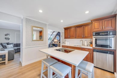 Kitchen with stainless steel appliances, a breakfast bar, brown cabinets, wallpapered walls, and a wainscoted wall