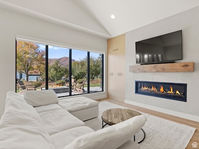 Living area with vaulted ceiling, light wood finished floors, recessed lighting, and a glass covered fireplace