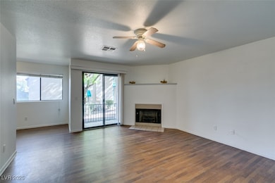 Unfurnished living room with wood finished floors, a fireplace, a ceiling fan, and a textured ceiling