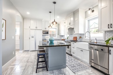 Kitchen with white cabinets, dark stone counters, built in appliances, a kitchen island, and hanging light fixtures