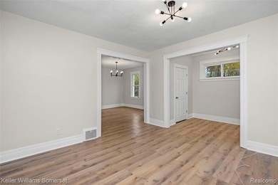 Unfurnished room featuring a chandelier, light wood-type flooring, and a textured ceiling