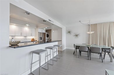 Kitchen with stacked washer / drying machine, tasteful backsplash, a kitchen breakfast bar, and white cabinetry